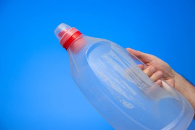 Kafkas erkek eli, mavi arka plan stüdyo çekiminde içi çiğ ve damlacıklarla dolu büyük boş bir plastik şişe tutuyor..