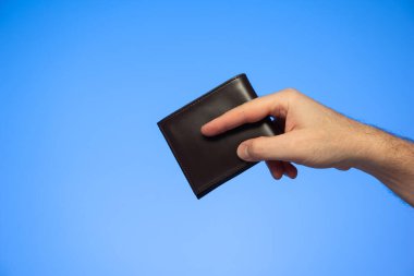 Beyaz erkek, elinde siyah deri bir cüzdan var. Mavi üzerine izole edilmiş bir jest stüdyosu çekimi yapıyor..