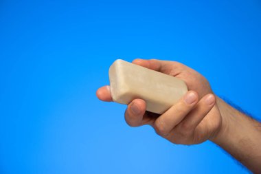 Beyaz tenli birinin elinde tuttuğu bir kalıp sabun mavi arka plan stüdyo çekimlerinde izole edilmiş..