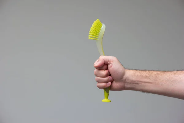 Green rubber plastic kitchen cleaning brush held in hand by Caucasian male hand isolated on gray background.
