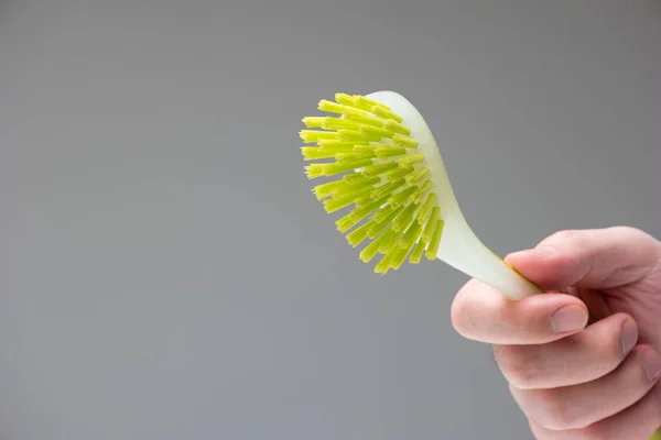 Green rubber plastic kitchen cleaning brush held in hand by Caucasian male hand isolated on gray background.