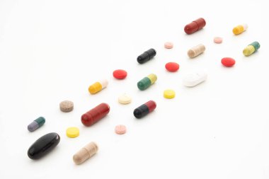 Beyazlar üzerine izole edilmiş sıra sıra dizilmiş çeşitli renkte tıbbi haplar ve kapsüller..