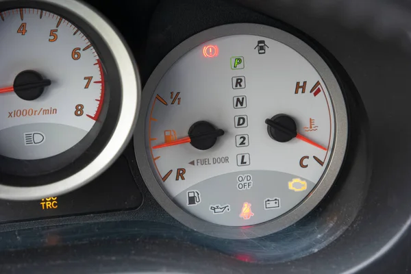 Car gauge dials showing glowing check engine light and seat belt reminder light symbols close up shot.