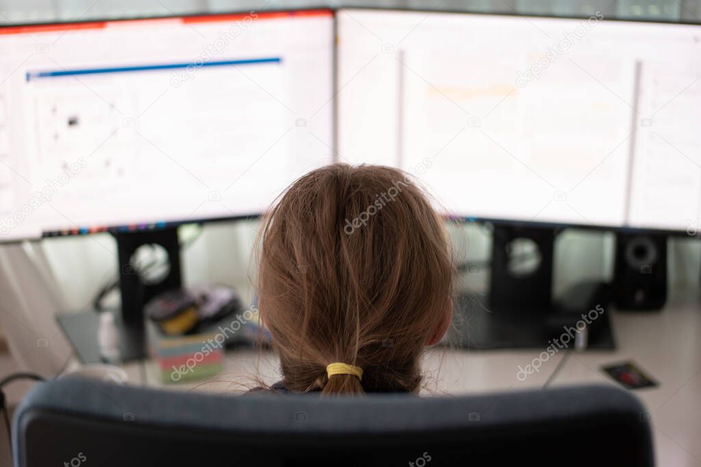 Unrecognizable Caucasian young woman working on the computer from home office with 2 blurry display monitors close up shot shallow depth of field.