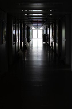 Kapalı bina koridoru, uzaktaki cam kapıya açılıyor. Dışarıda gün ışığı var, insan yok..