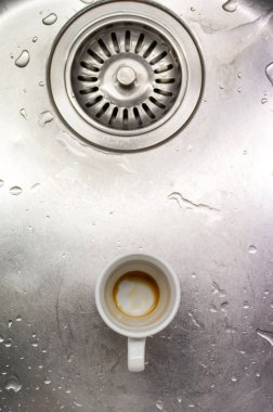 Küçük beyaz porselen kirli kahve fincanı. Metal mutfak lavabosunun yanında. Delik üst görünümü için..