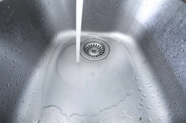 Akan musluk suyu, metal mutfak lavabosuna akıyor. Uzun pozlama, insan yok, geniş açı..