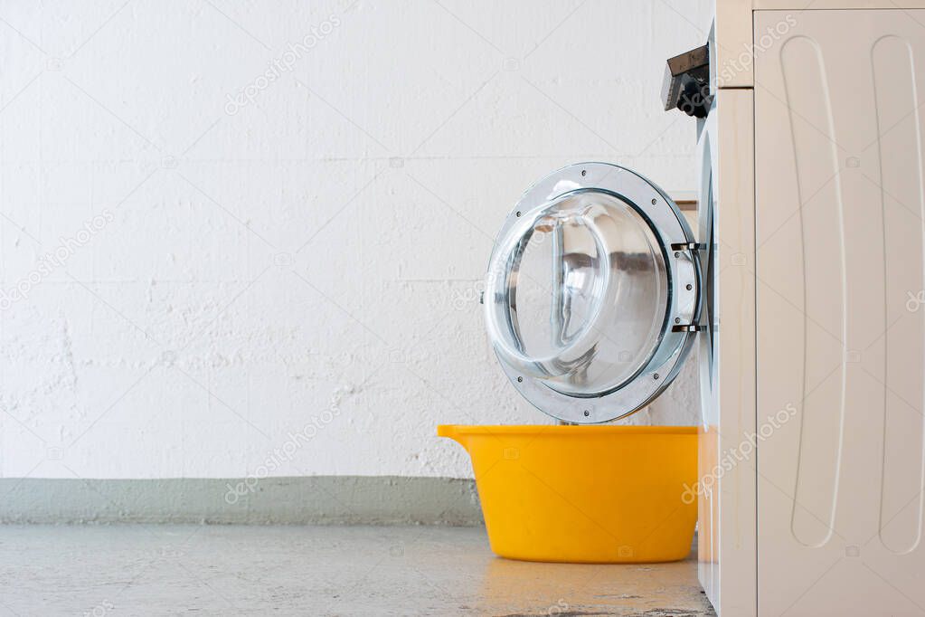 Landry room washing machine open door and yellow plastic basket. Side view no people.