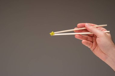 Beyaz erkek eliyle tutulan ahşap çubukların üzerinde taze yeşil Wasabi macunu. Stüdyoyu kapat, gri üzerine izole edilmiş..