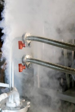 Metal borular ve kırmızı el vanalarına bağlı basınçlı tanktan çıkan sıvı nitrojen gazı..
