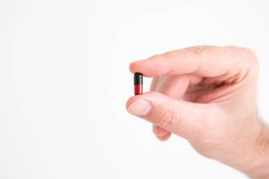 Kafkas erkek eli parmaklarının arasında tıbbi siyah ve kırmızı kapsül hapı tutuyor. Stüdyo çekimini kapat, beyaz arkaplanda izole edilmiş..