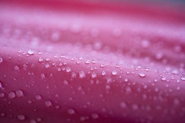 Su geçirmez ya da itici, koyu pembe tekstil kumaşlı su damlacıkları. Yaklaş, makro çekim, yüzeysel alan derinliği, insan yok.