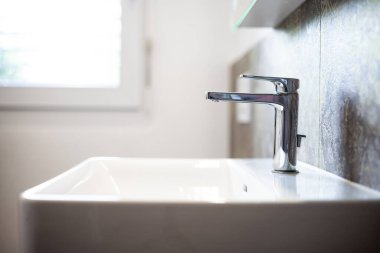 Modern kare banyo lavabosu ya da lavabo ve krom su musluğu. Geniş açı, kenar görüş, sığ alan derinliği, doğal pencere ışığı, insan yok.