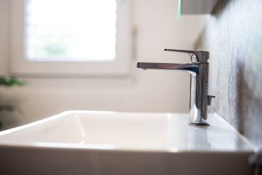 Modern kare banyo lavabosu ya da lavabo ve krom su musluğu. Geniş açı, kenar görüş, sığ alan derinliği, doğal pencere ışığı, insan yok.