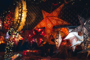 Aydınlatılmış kağıt yıldız fenerleri karanlık bir ortamda asılı duruyor. Yakın çekim, insan yok.