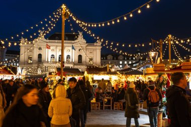 Zürih, İsviçre, 20 Kasım 2025. Sechselautenplatz Noel pazarındaki mağazaları ve tezgahları çok sayıda insan ziyaret ediyor. Mavi saat, geniş açı manzarası, ipe asılan ışıklar.