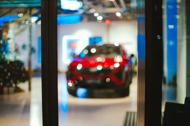 Bulanık, kırmızı, dağıtıcı galerisinde gece vakti yeni bir araba. Dışarıdan çekime bakıyor, soyut bir arkaplan, insan yok.