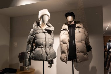 Moda mağazasının vitrininde şık kışlık ceketli iki manken var. Aydınlatılmış dükkan penceresi, gece fotoğrafı, insan yok.