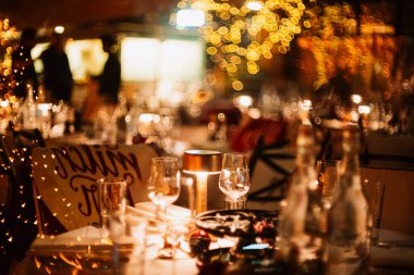 Bokeh ışıkları olan boş, şenlikli bir yemek masası. Huysuz, romantik atmosfer, çok sığ alan derinliği, insan yok.