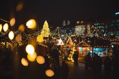 Zürih HB, İsviçre, 5 Aralık 2025. Geceleyin Sechselautenplatz Noel Pazarı. Tezgahları ve çekimleri ziyaret eden insanlar, yukarıdan bakıldığında, ön planda bokeh topu vurgusu var.