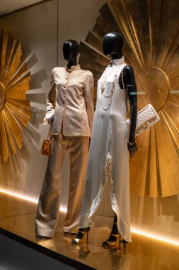 Zürih, İsviçre, 12 Aralık 2025. Chanel Lisesi moda mağazası vitrininde iki siyah manken altın bir takım elbise ve beyaz elbise giyiyor. Gece çekimleri, insan yok.
