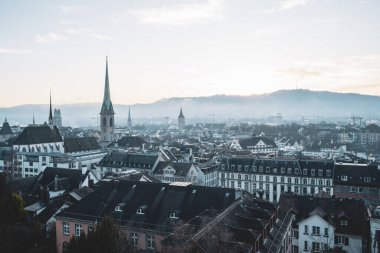 Zürih, İsviçre, 18 Aralık 2025. Sisli bir kış sabahı eski şehir merkezinin manzarası yükseldi. Çatı perspektifi, geniş açı görünümü, arka planda Uetliberg