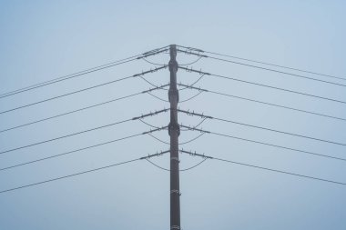 Sisli gökyüzüne karşı yüksek voltajlı elektrik iletim pilonu. Yukarıya bakıyorum, kimse yok.