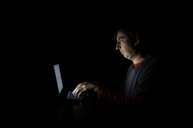 Karanlık bir odada dizüstü bilgisayarıyla aydınlatılmış beyaz bir adam. Yan görünüş, zifiri karanlık oda