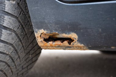 Şiddetli pas hasarı ve paslanma deliğine yakın. Tekerlek kemerinin yanındaki koyu gri sallanan panelde çürümüş metal ve soyulmuş boyayı gösteriyor..