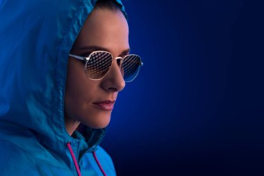 Kapüşonlu ve koyu mavi arka planda güneş gözlüğü takan genç bir kadının portresi..
