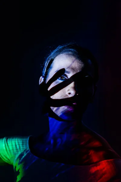 Koyu arkaplanda renkli ışıklarla aydınlatılmış yaratıcı bir kadın portresi..