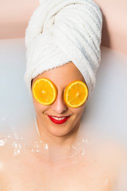 Kafasında havluyla beyaz bir kadın, küvette süt ile banyo yapıyor. Vücut bakımı kavramı.