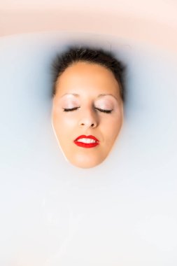 Beyaz bir kadın, içi süt dolu bir küvette banyo yapıyor. Vücut bakımı kavramı.