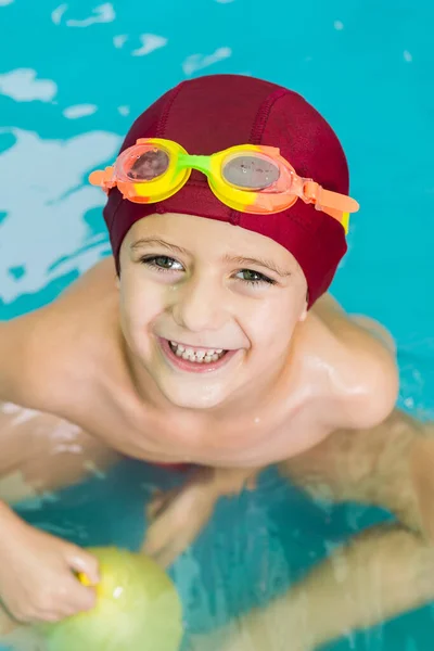 Portrait of a smiling child with a red swimming cap, in a small rubber pool, playing with water balloons. Summer is the ideal time for water games.