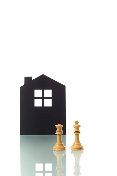 İki beyaz satranç taşının (kral ve kraliçe) kavramsal fotoğrafı, arka planda bir evin silueti olan, çocuksuz beyaz heteroseksüel bir çifti metaforik olarak temsil etmektedir. Kopyalamak için boşluk.