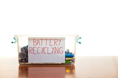 Beyaz arka planı olan tahta bir masada içi batarya dolu bir konteynır. Geri dönüşüm ve çevre bakımı kavramı. Boşluğu kopyala.