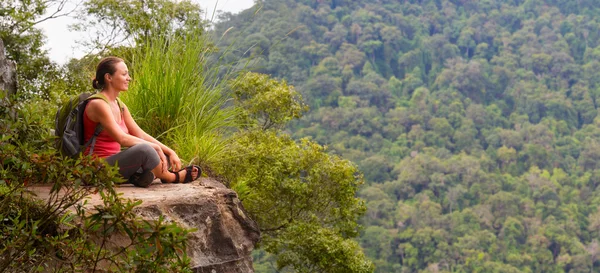 Mujer excursionista se sienta en el borde del acantilado y disfrutar de tropical — Foto de Stock