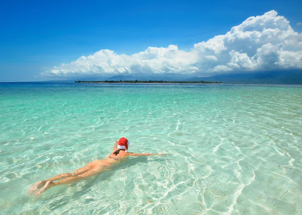 Nő visel bikini Santa kalap és úszni a vízben strandon. — Stock Fotó