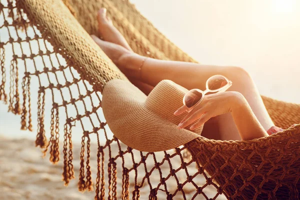 Πόδια και το χέρι χαλαρωτική γυναίκα στην αιώρα στην παραλία κατά τη διάρκεια του ηλιοβασιλέματος. — Φωτογραφία Αρχείου