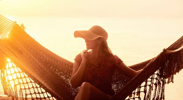 Wakacje Beach Summer Holiday Concept. Młoda piękna kobieta w kapeluszu siedzi w hamaku o zachodzie słońca — Zdjęcie stockowe