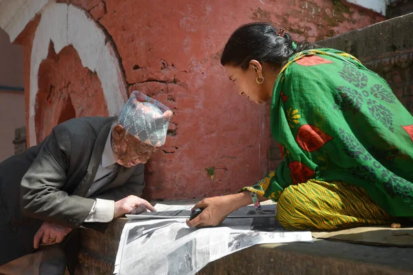 Katmandú, Nepal - 14 de octubre de 2017: Un indio le lee un periódico a una mujer en una calle de la ciudad de Katmandú. Imágenes De Stock Sin Royalties Gratis