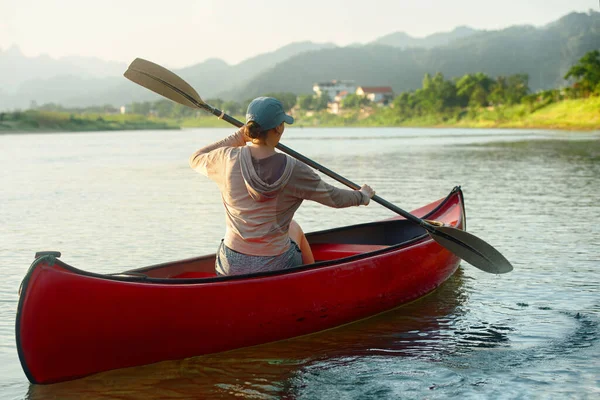 Mujer remando remos mientras flota en kayak en el río sobre el fondo de las casas en el campo. — Foto de Stock