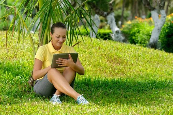 Mujer joven usando tableta al aire libre acostado en la hierba, sonriendo —  Fotos de Stock
