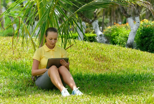 Jonge vrouw met behulp van Tablet PC buiten opleggen van gras. — Stockfoto