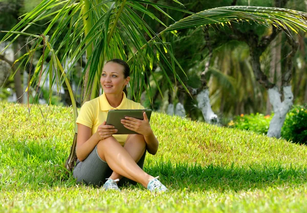 Jovem mulher usando tablet deitado ao ar livre na grama, sorrindo . — Fotografia de Stock