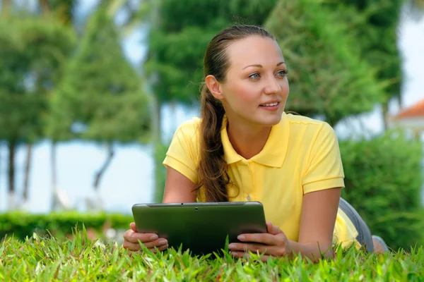 Jonge vrouw op het gazon onder een palmboom met haar tablet comput — Stockfoto