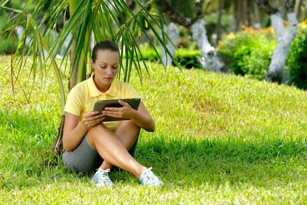 Jovem mulher no gramado sob uma palmeira com seu tablet comput — Fotografia de Stock