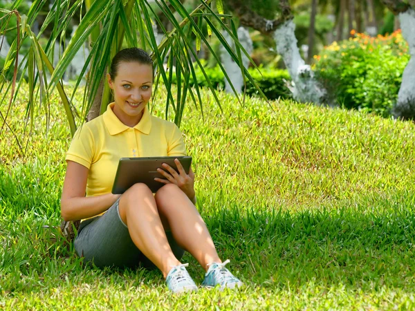 Jovem mulher usando tablet deitado ao ar livre na grama, sorrindo . — Fotografia de Stock