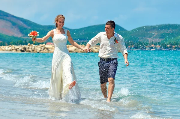 Счастливая невеста и жених, бегущий по красивому пляжу — стоковое фото