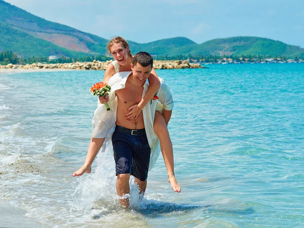 Lyckliga bruden och brudgummen som körs på en vacker tropisk strand — Stockfoto